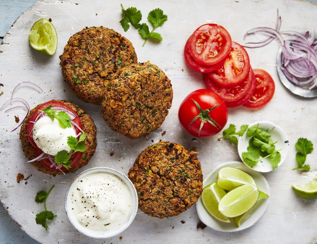 A close-up of flatbreads topped with sliced tomatoes, onion, and a dollop of yogurt, garnished with fresh cilantro and lime wedges, arranged on a rustic white plate.